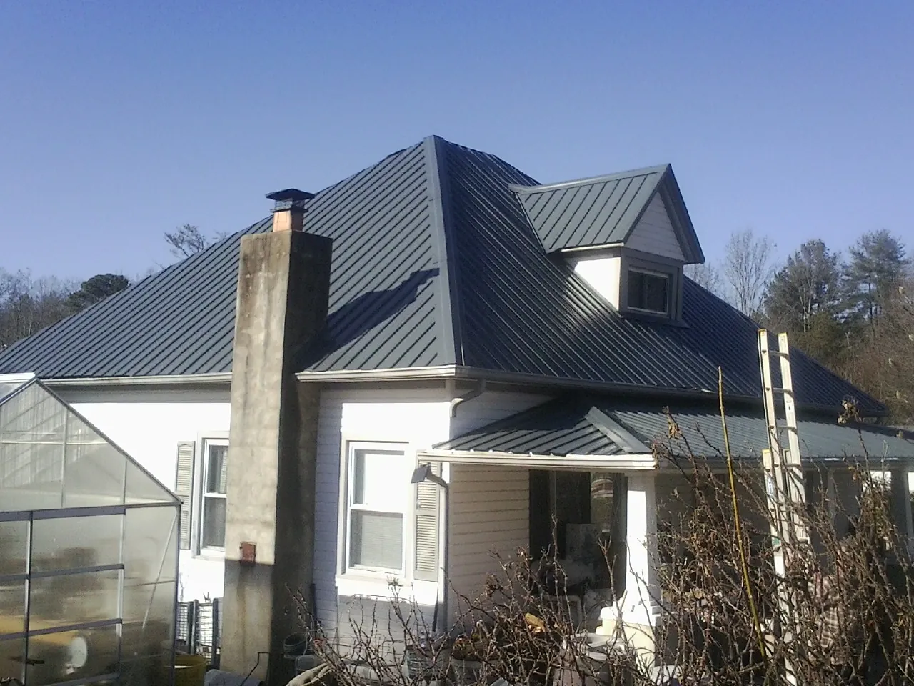 Dark blue standing seam metal roof on a white farmhouse with dormer — Slate & Tile Roof Repair by Roofing Brothers in Center Rutland