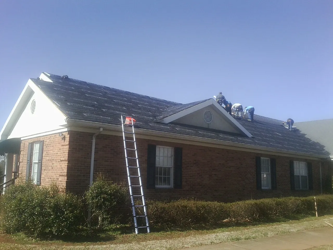 Crew tearing shingles off a brick ranch roof with a ladder set — Emergency Roof Repair work by our crew in Center Rutland