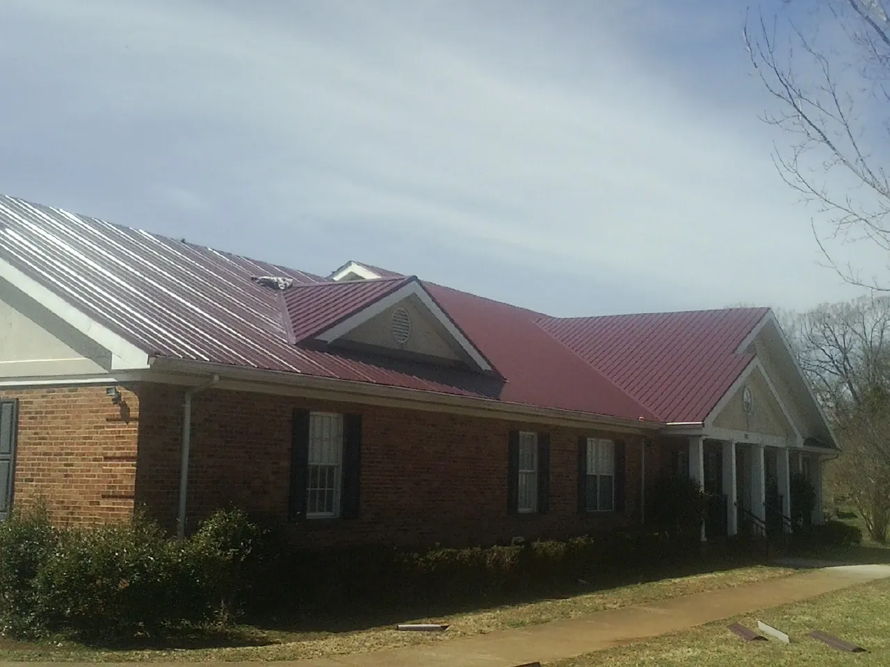 Red metal roof with gabled entries on a long brick building, from a Hail Damage Roof Repair job in Center Rutland