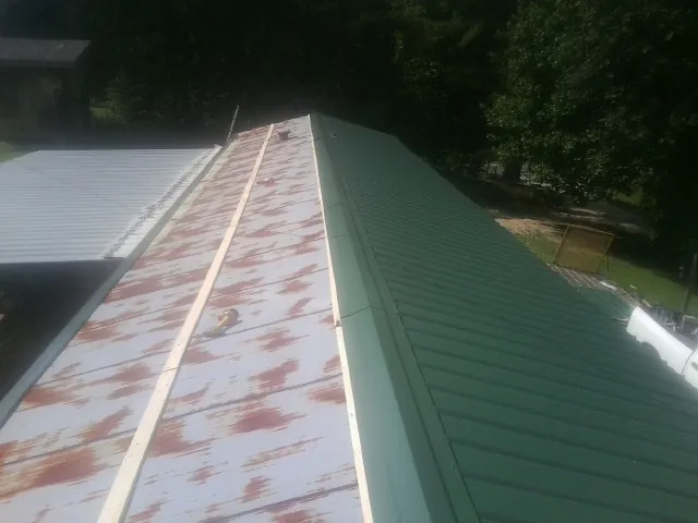 Old rusted panels beside newly installed green metal roofing — Wind Damage Roof Repair by Roofing Brothers in Center Rutland
