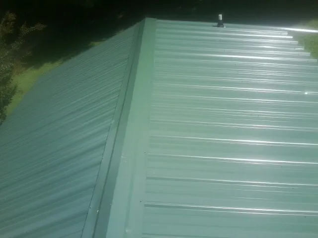 New green metal panels meeting at the ridge of a roof — Flat Roof Repair work by our crew in Center Rutland