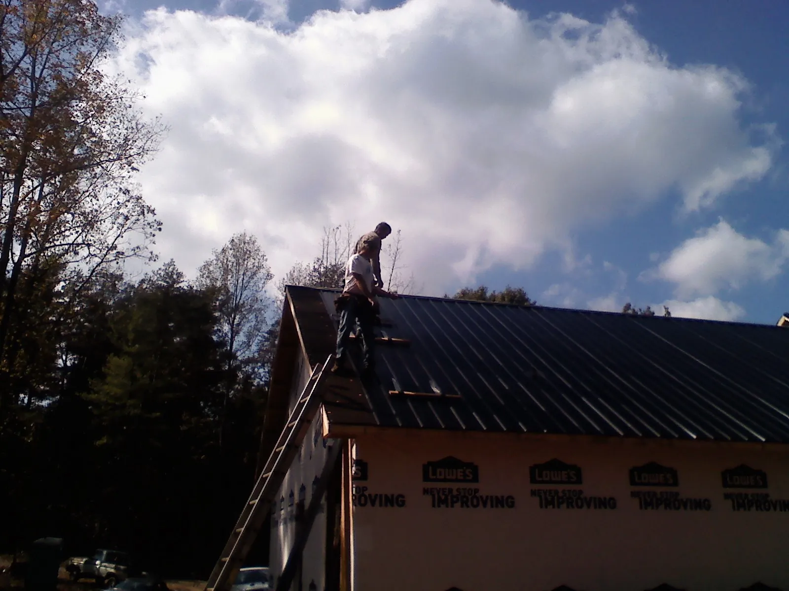 Roofer fastening dark metal panels high against a cloudy sky, from a Roof Inspection job in Center Rutland