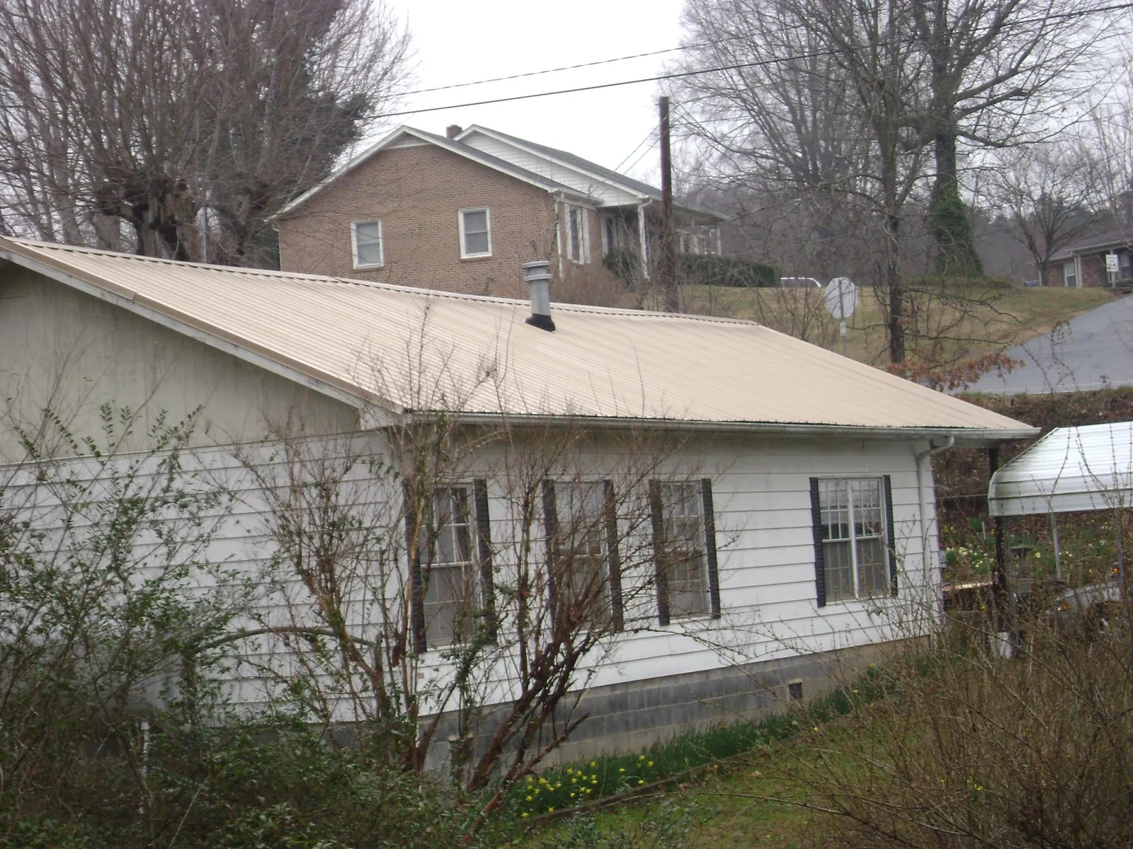 Tan metal roof on a white sided house set into a hillside — Commercial Roofing by Roofing Brothers in Center Rutland